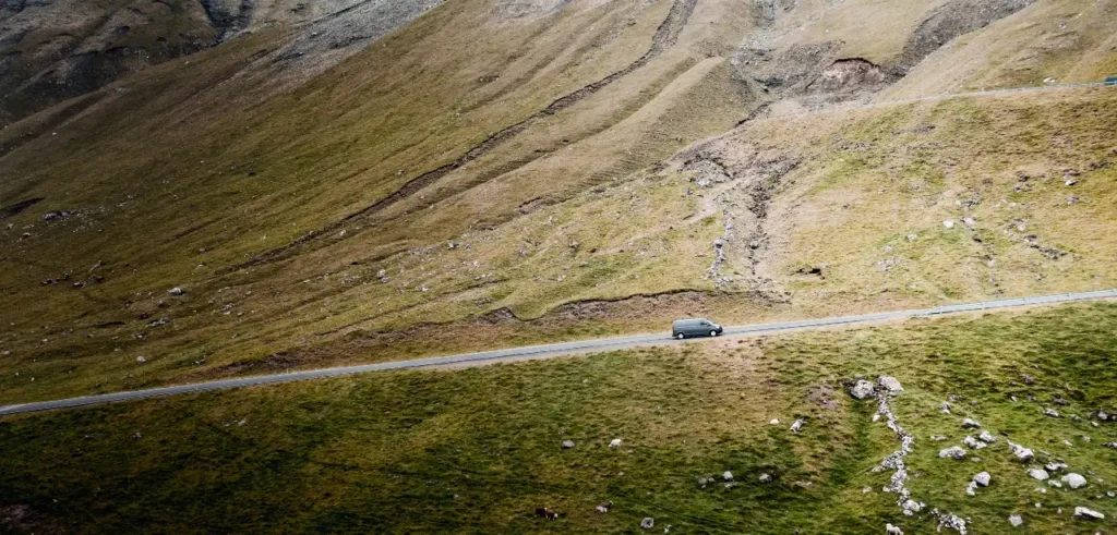 Camper van driving uphill on a mountain road in the Faroe Islands