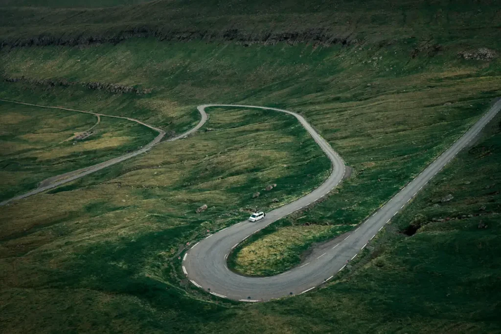 A-long-and-winding-road-in-Faroe-Islands White camper van driving on a winding mountain road through green hills in the Faroe Islands