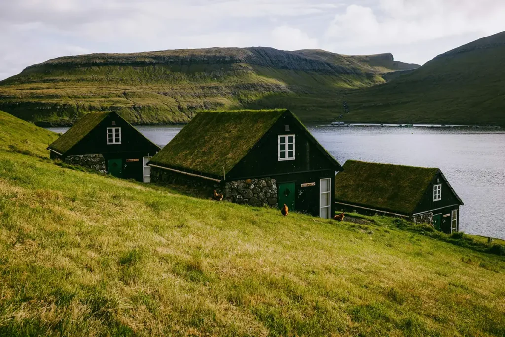 Traditional grass-roof houses on a hillside overlooking a lake and mountains in the Faroe Islands