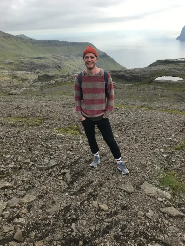 Smiling hiker standing on rocky terrain in the Faroe Islands with ocean and cliffs in the background
