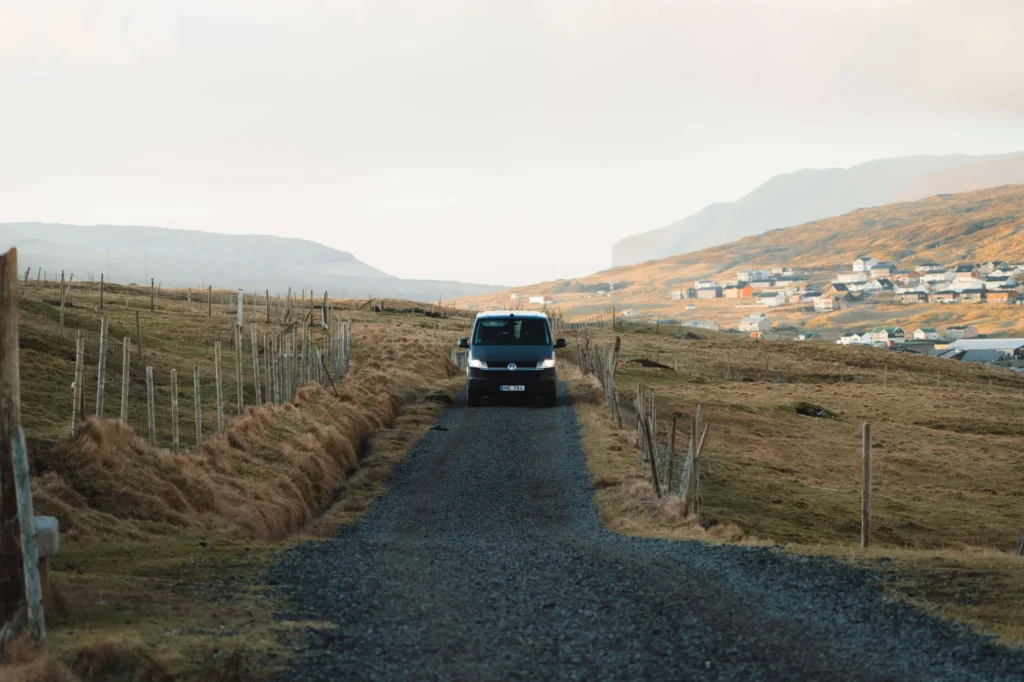 Campervan driving on a rural road in the Faroe Islands near a small village