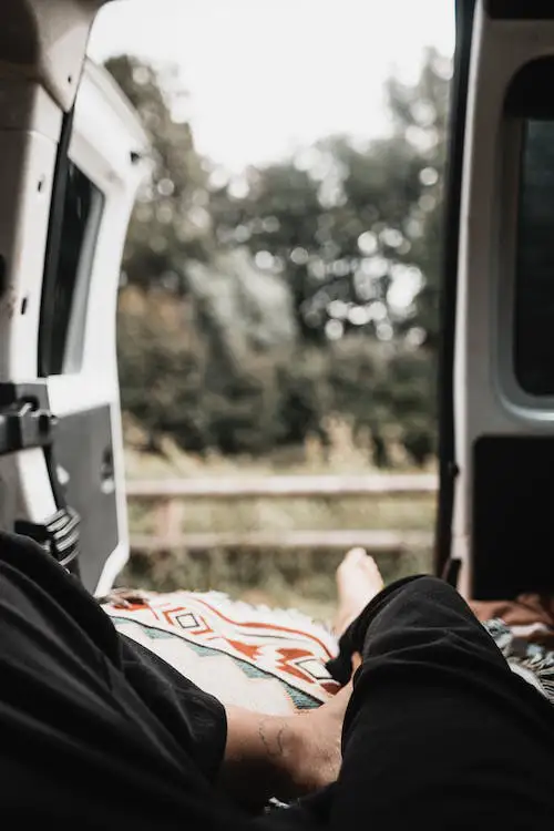 Person lying inside a campervan with doors open, looking out at nature