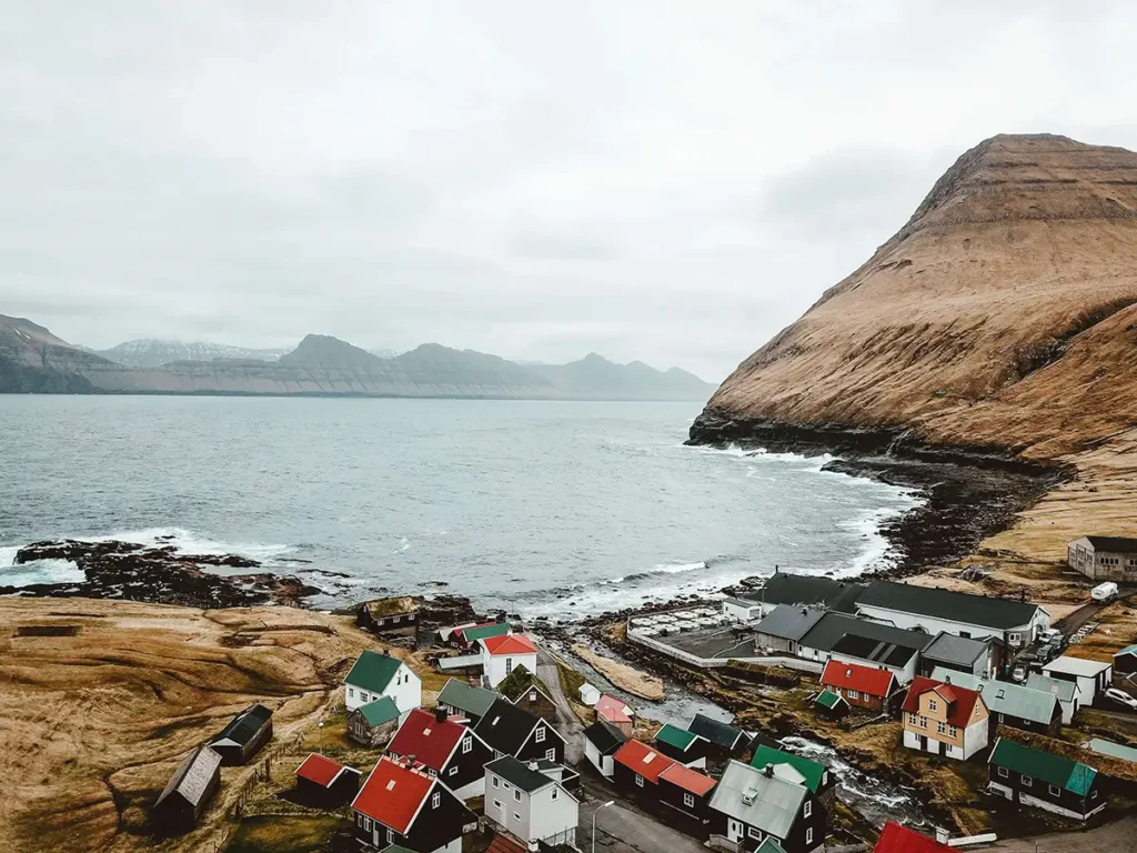 City-Of-Klaksvik Aerial view of a coastal village with colorful houses, steep cliffs, and the ocean in the Faroe Islands