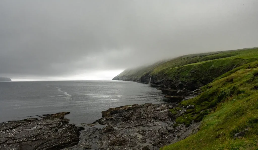 Misty coastline with rocky shore and green cliffs in the Faroe Islands