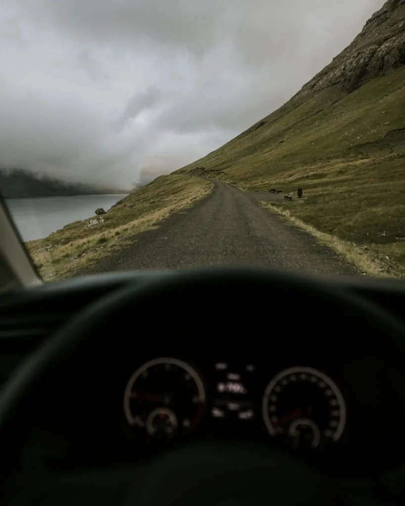 Driver’s view of a narrow coastal road through misty green hills in the Faroe Islands