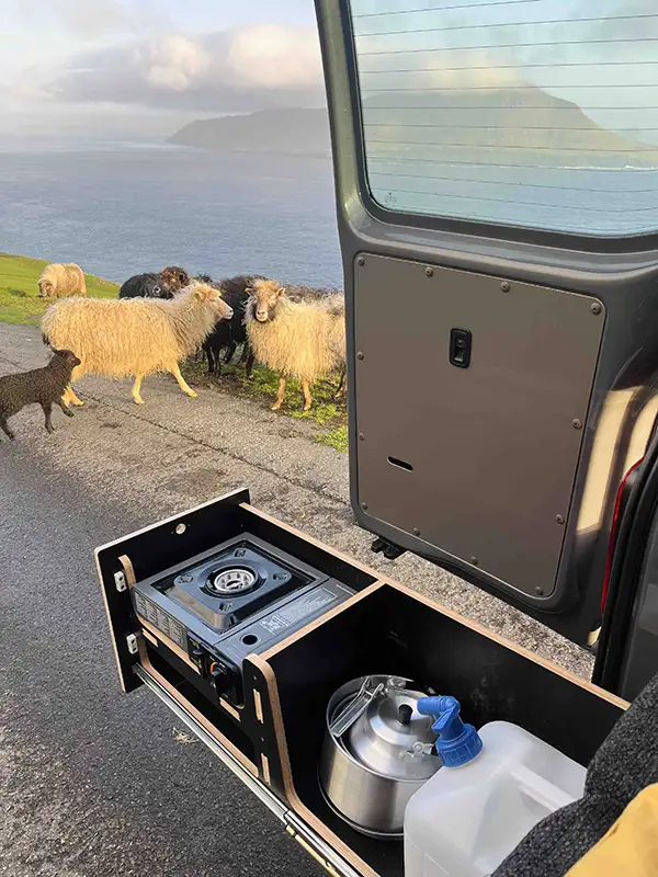 Compact campervan outdoor kitchen setup with sheep nearby in the Faroe Islands