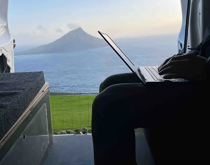 Working on a laptop inside a campervan with ocean and mountain view in the Faroe Islands