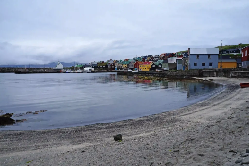 Colorful seaside village and calm harbor on the island of Nólsoy in the Faroe Islands, viewed from a quiet sandy beach
