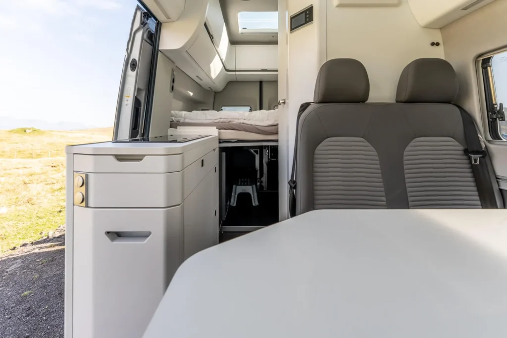 Modern campervan interior with swivel seats, dining table, compact kitchen and rear bed
