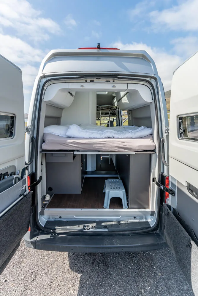 Interior view of a VW campervan with rear doors open, showing bed and compact camper layout