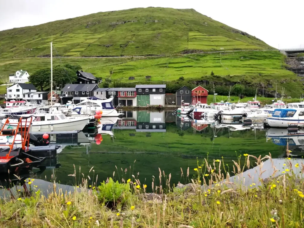 Boats docked at Vestmanna Harbour with colorful houses and green hills reflected in the water, Faroe Islands