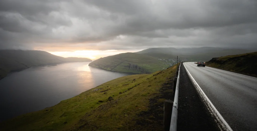 Coastal road overlooking a calm fjord at sunset with dramatic clouds in Vestmannasund, Faroe Islands