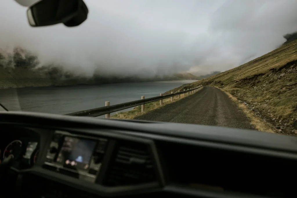 Driving along a foggy coastal road in the Faroe Islands with mountains and water in view