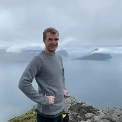 Bartal Kamban standing on a cliff with an ocean and mountains in the background on the Faroe Islands