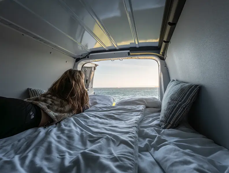 Woman relaxing inside a camper van with an ocean view on the Faroe Islands