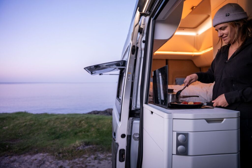 Woman cooking inside a campervan overlooking the Faroe Islands coastline
