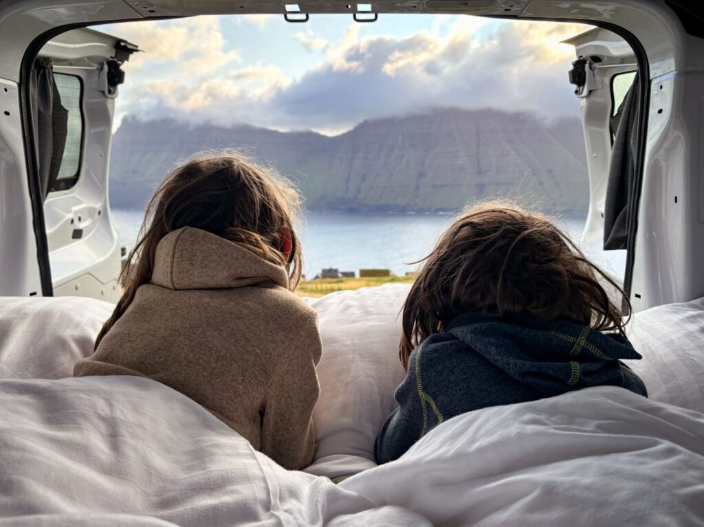 Children relaxing inside a campervan with mountain view in the Faroe Islands