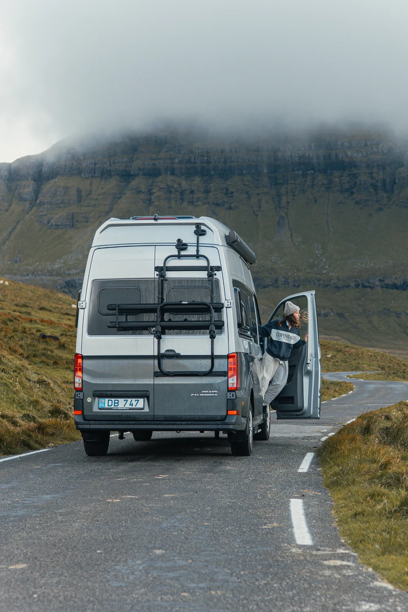 Traveller standing in the open doorway of a campervan beneath misty Faroese mountains.