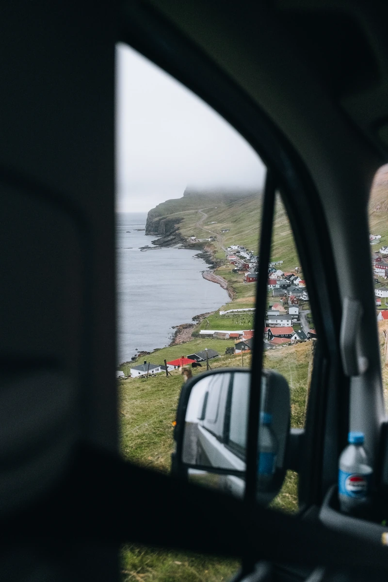 Coastal village and green hills seen through a campervan side window in the Faroe Islands.